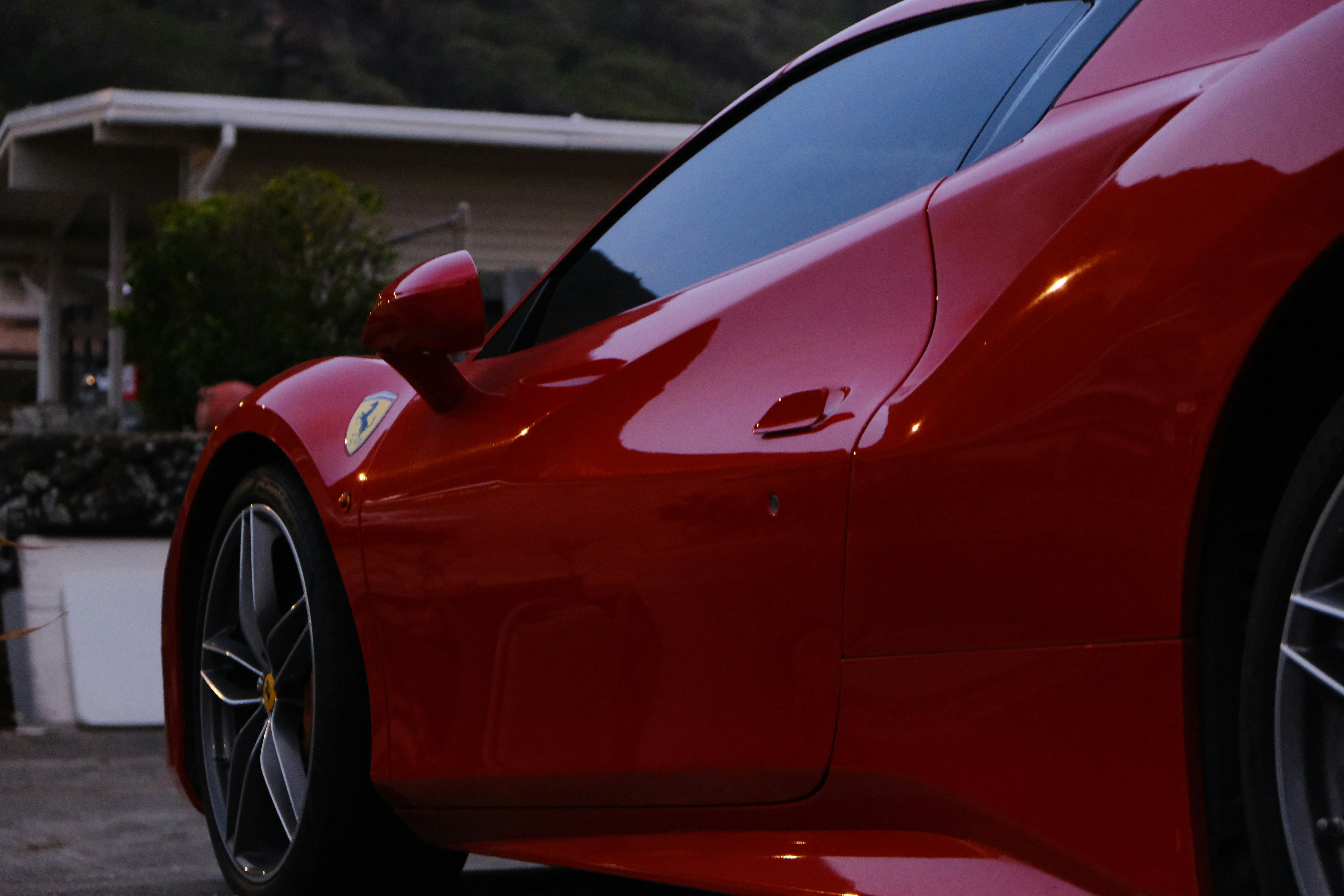 Red sports car freshly detailed on a residential street, mirror-like paint reflecting surrounding trees and sky