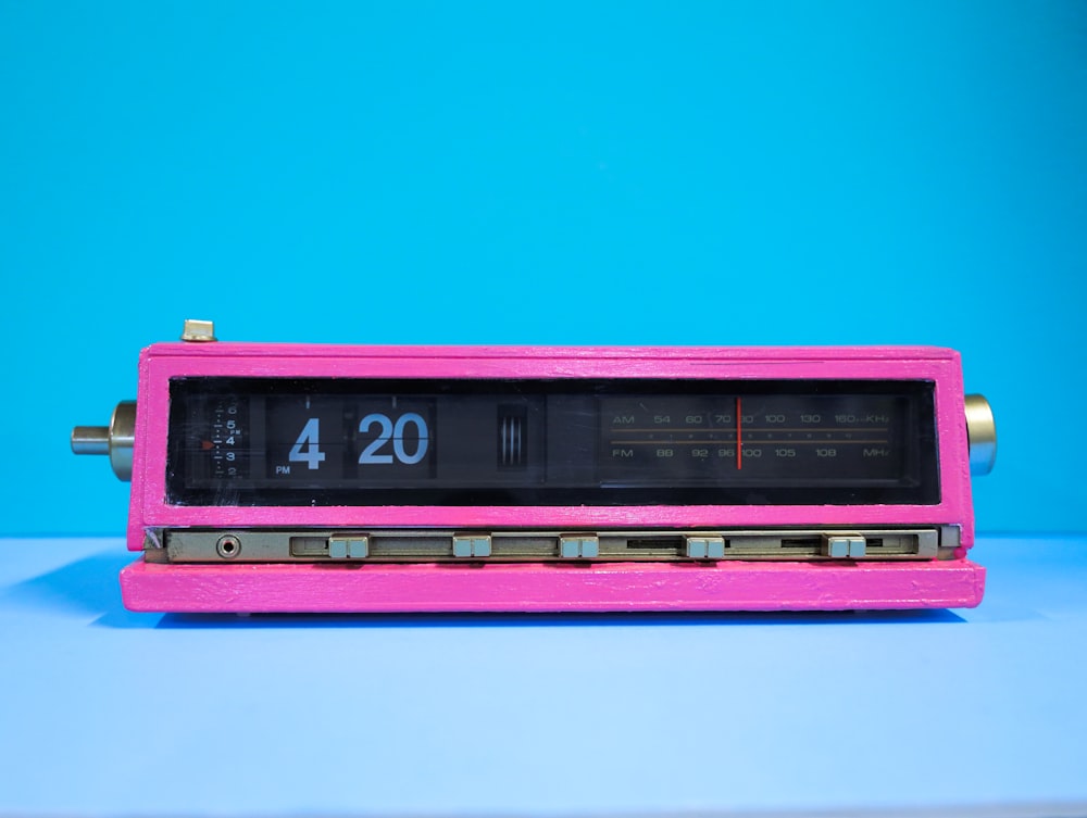 a pink radio on a blue table with blue background displays the time 4:20