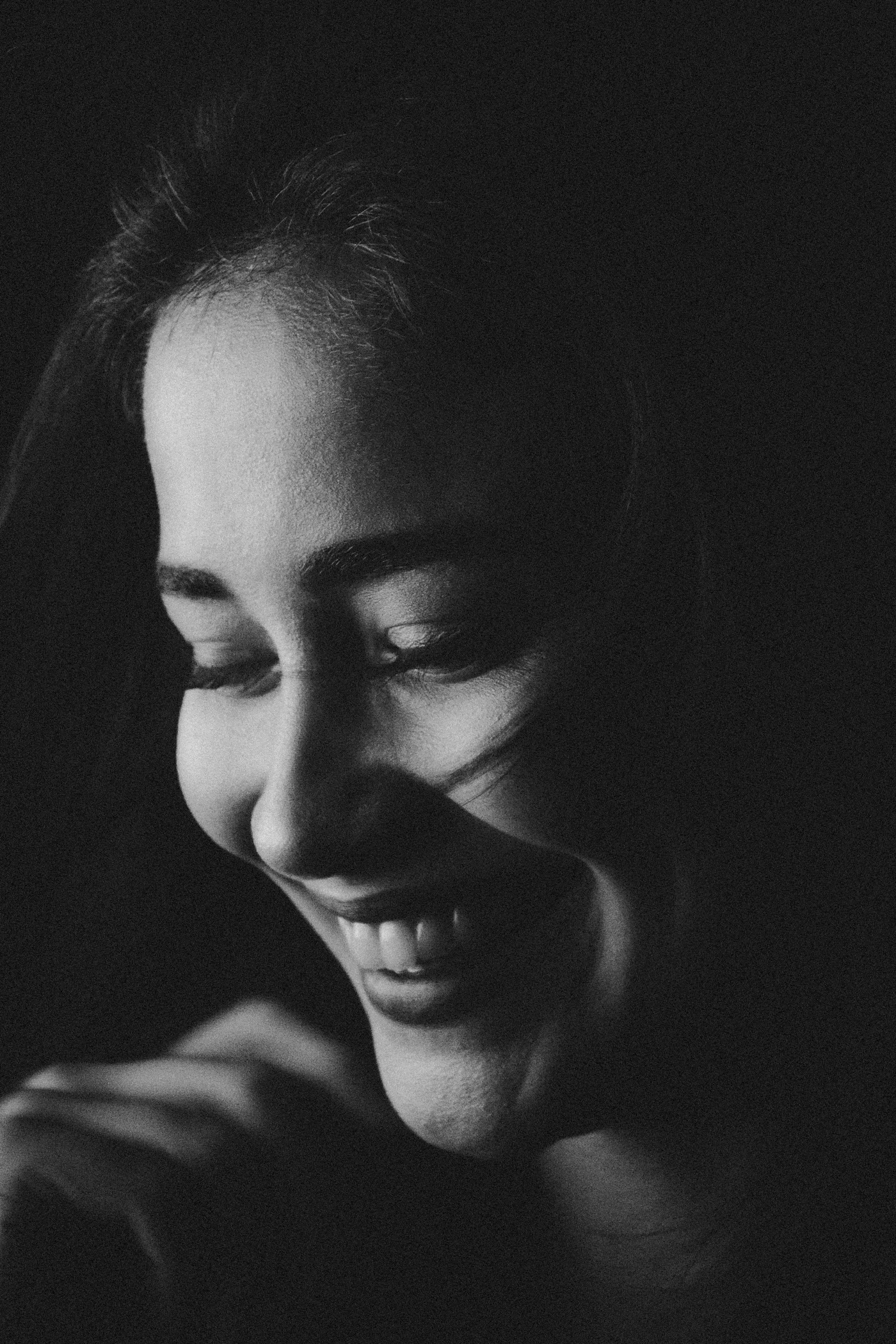 Black-and-white portrait of a smiling woman looking downward, with her face and teeth clearly visible.