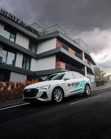 A sleek, modern electric SUV parked in front of a glass office building under soft daylight.