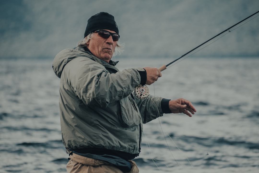 man in gray jacket and black cap holding fishing rod