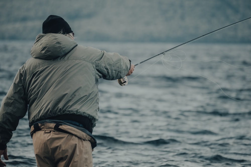man in gray jacket and blue denim jeans holding black fishing rod