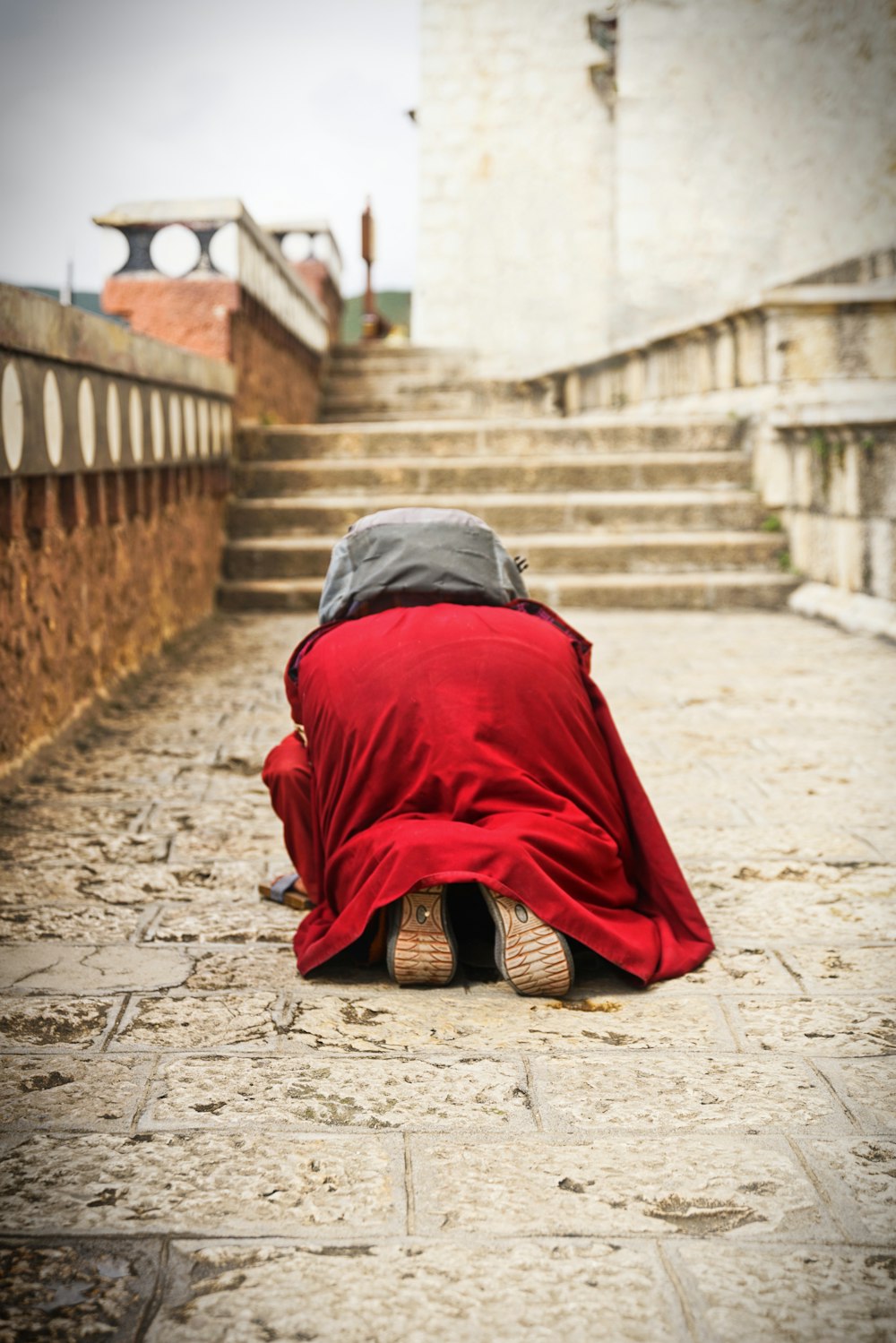 person in red and black robe sitting on brown concrete stairs