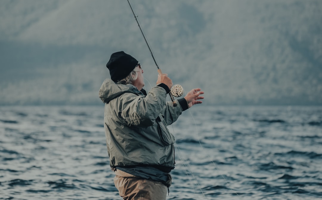 man in green jacket and brown pants fishing on sea during daytime