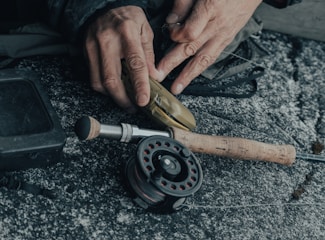 A skilled technician carefully repairing a fishing reel in a clean, organized workshop with fishing gear around.