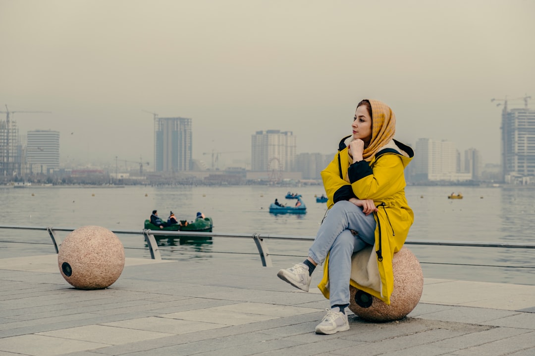woman in yellow hoodie sitting on brown rock near body of water during daytime