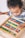 A young child is engaged with a colorful wooden abacus, focusing intently on the counting beads. The abacus features rows of alternating colors with beads in red, blue, green, yellow, and white. The child appears curious and concentrated as they manipulate the beads.