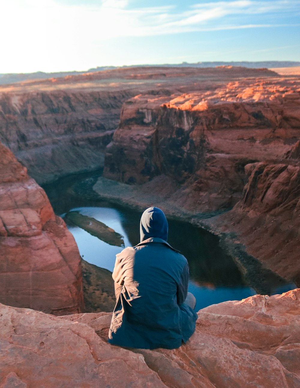 man in blue jacket and brown pants sitting on brown rock formation during daytime