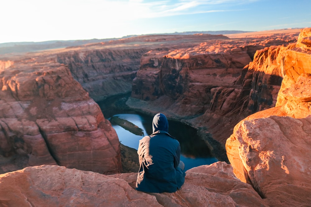 man in black jacket sitting on brown rock formation during daytime