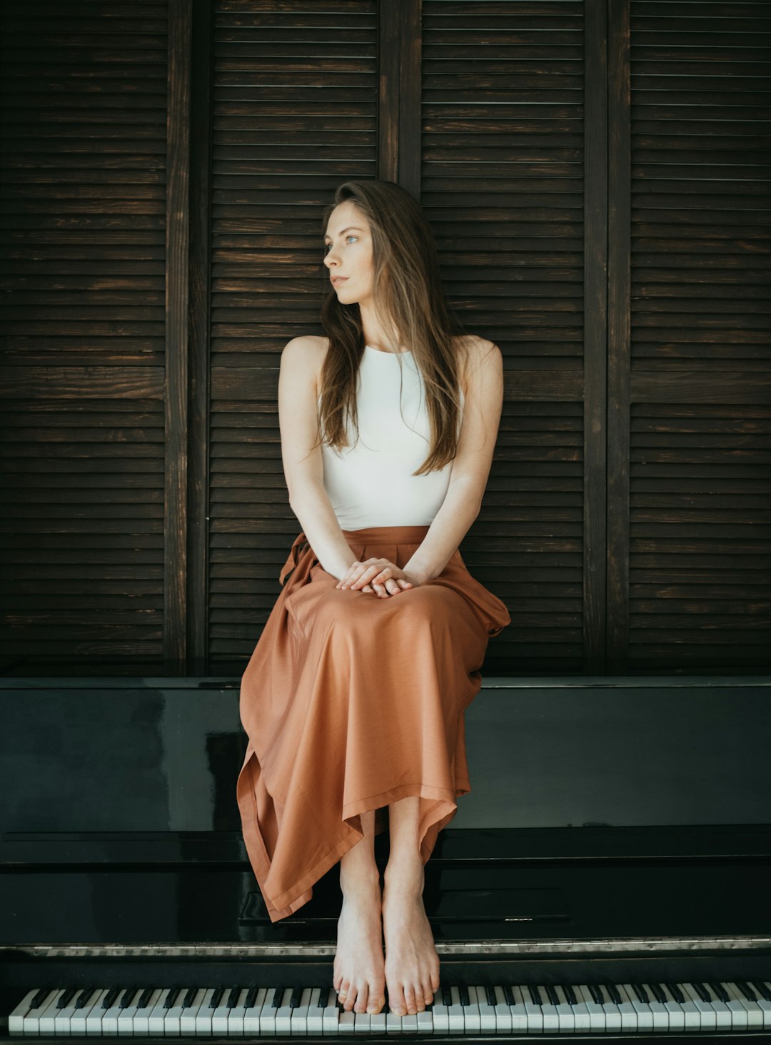 woman in white tank top and orange skirt standing in front of brown wooden wall
