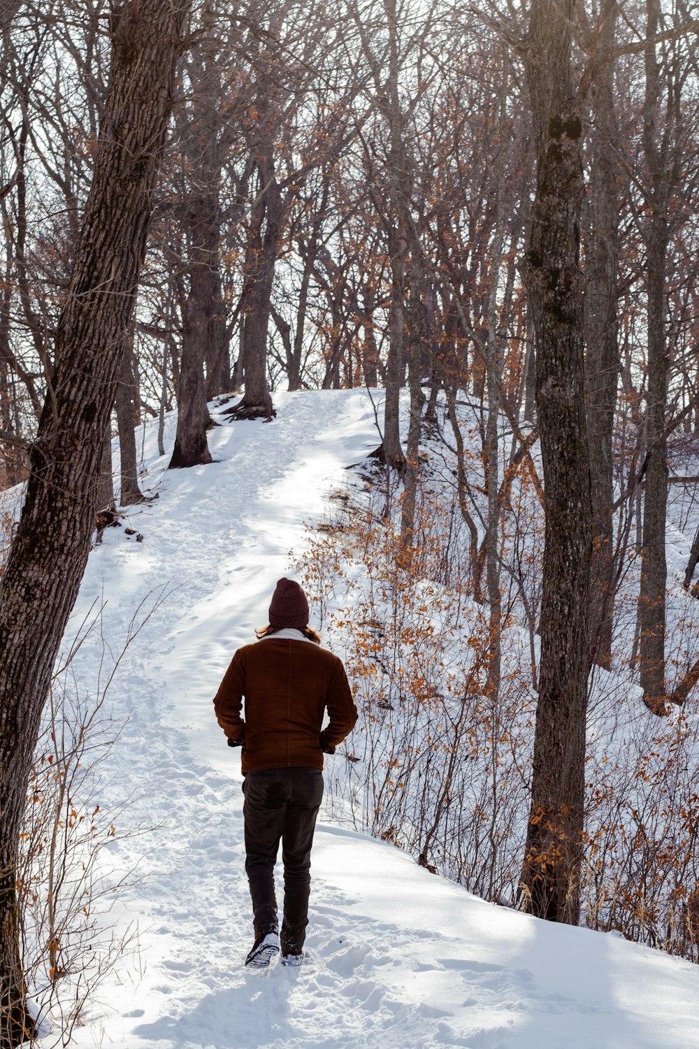 man in brown jacket and black pants standing on snow covered ground during daytime