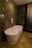 A modern bathroom featuring a sleek, freestanding bathtub with a curved design. The walls and floor have a marble finish in various shades of brown, enhancing the luxurious feel. A white towel is draped over the side of the tub, and there is a polished silver faucet nearby. The ambient lighting casts soft reflections on the marble surfaces.