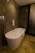 A modern bathroom featuring a sleek, freestanding bathtub with a curved design. The walls and floor have a marble finish in various shades of brown, enhancing the luxurious feel. A white towel is draped over the side of the tub, and there is a polished silver faucet nearby. The ambient lighting casts soft reflections on the marble surfaces.