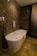 A modern bathroom featuring a sleek, freestanding bathtub with a curved design. The walls and floor have a marble finish in various shades of brown, enhancing the luxurious feel. A white towel is draped over the side of the tub, and there is a polished silver faucet nearby. The ambient lighting casts soft reflections on the marble surfaces.