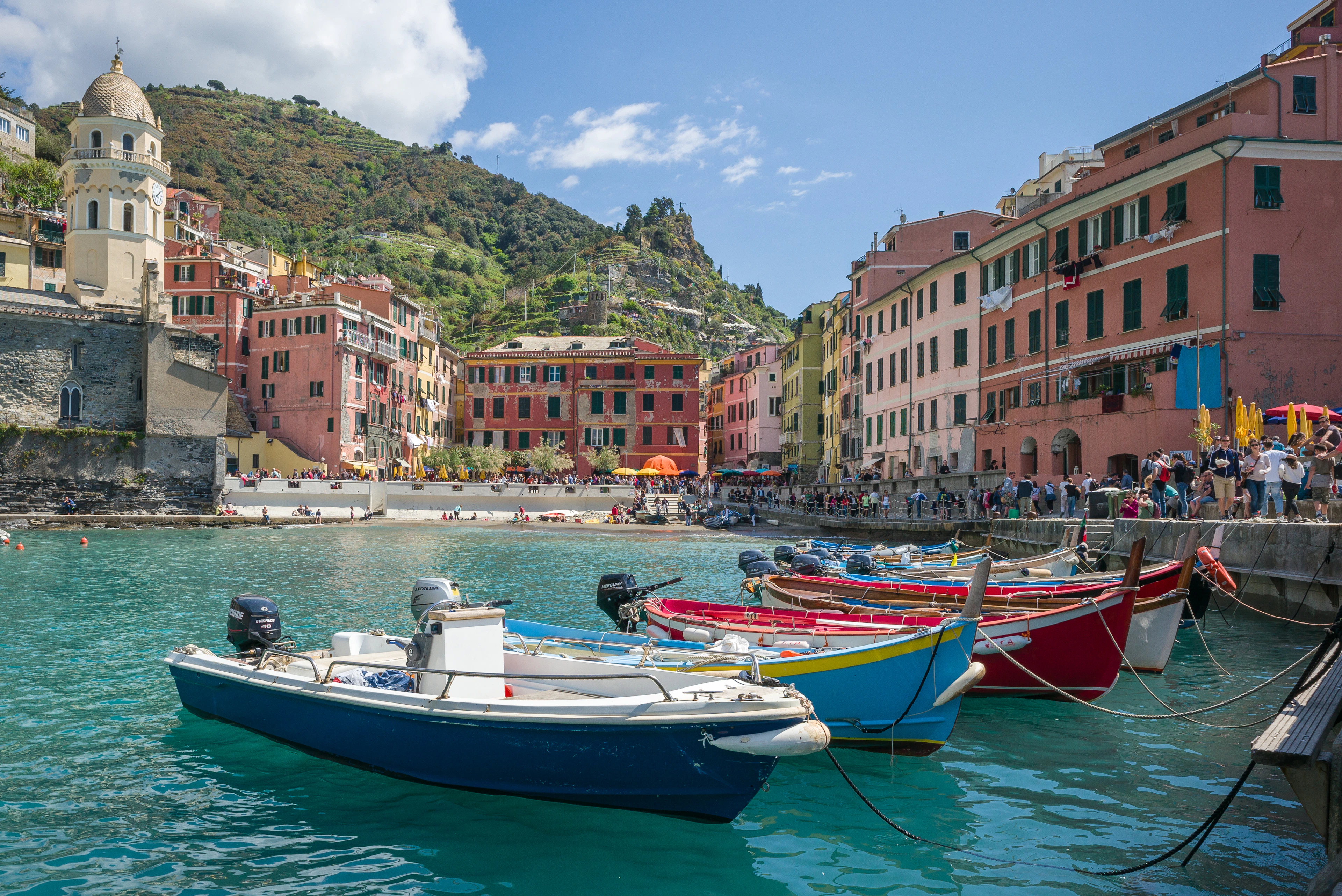 Brightly painted wooden boats moored in Vernazza's harbour, the village's tall pastel houses and church tower rising behind.