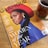 A magazine titled 'Glamour' featuring a stylish woman with a braided hairstyle, wearing a red hat and a blue outfit. It highlights the 'Women of the Year' issue and includes other notable names. A cup of tea with a sunflower design is placed beside the magazine on a wooden surface.