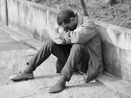 man in gray jacket and black pants sitting on concrete bench
