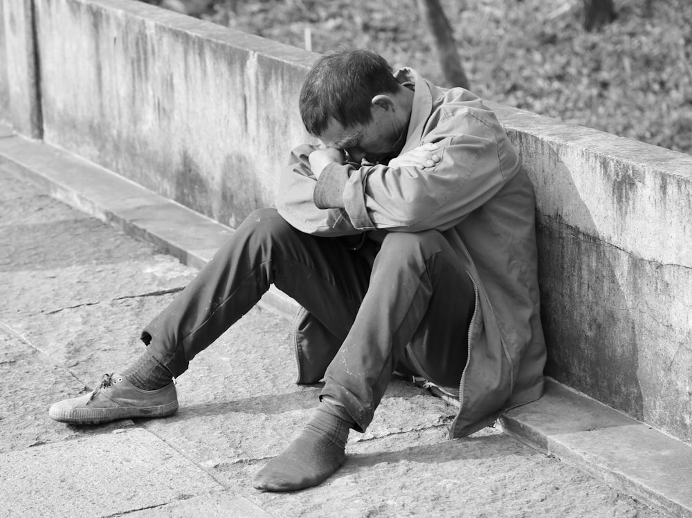 Hombre con chaqueta gris y pantalones negros sentado en un banco de hormigón