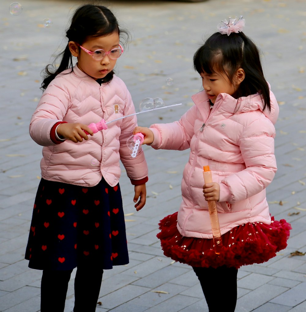 2 girls in pink long sleeve shirt standing on gray concrete floor during daytime