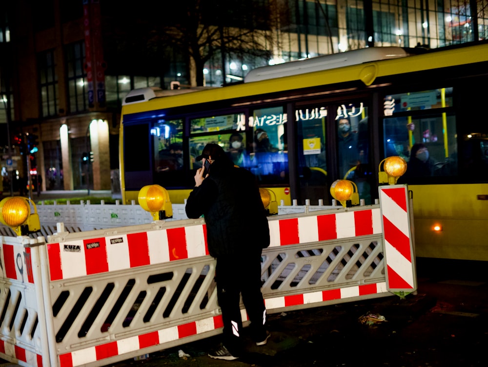 man in black jacket standing beside yellow and white bus during daytime