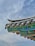 A traditional architectural roof with intricate designs is depicted, featuring colorful patterns in green, blue, red, and black. The roof is adorned with decorative tiles and carvings, all set against a backdrop of a cloudy sky.