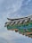 A traditional architectural roof with intricate designs is depicted, featuring colorful patterns in green, blue, red, and black. The roof is adorned with decorative tiles and carvings, all set against a backdrop of a cloudy sky.
