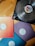 A turntable sits on a wooden surface, featuring a vinyl record with a label that has geometric designs. Nearby are three vinyl sleeves in red-orange, purple, and blue, each labeled 'Connected Vol. 3'. The overall composition suggests a musical theme.