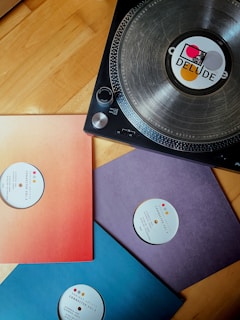 A turntable sits on a wooden surface, featuring a vinyl record with a label that has geometric designs. Nearby are three vinyl sleeves in red-orange, purple, and blue, each labeled 'Connected Vol. 3'. The overall composition suggests a musical theme.