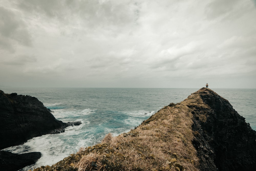 person standing on rock formation near sea under white clouds during daytime