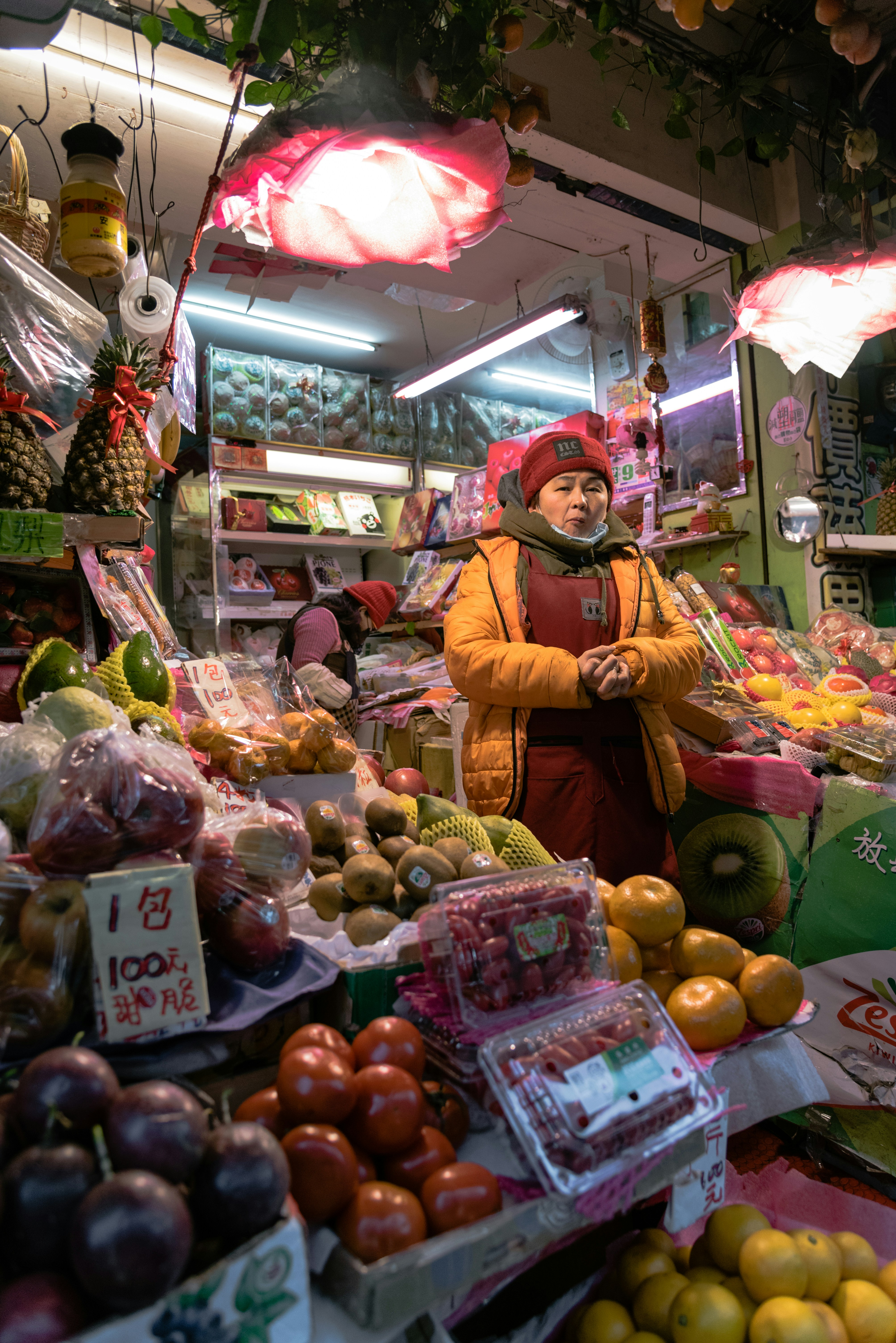 woman in yellow long sleeve shirt standing in front of fruit stand