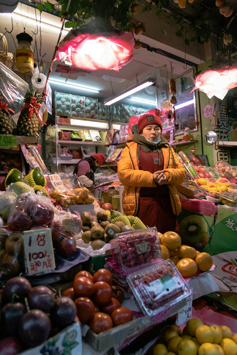 woman in yellow long sleeve shirt standing in front of fruit stand