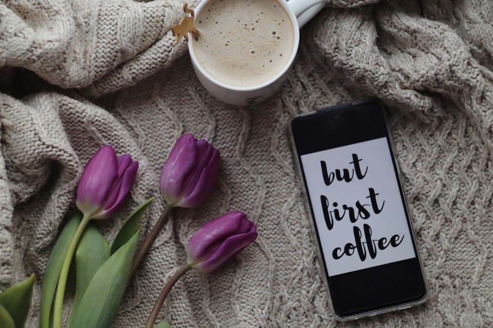 black smartphone beside white ceramic mug on white textile