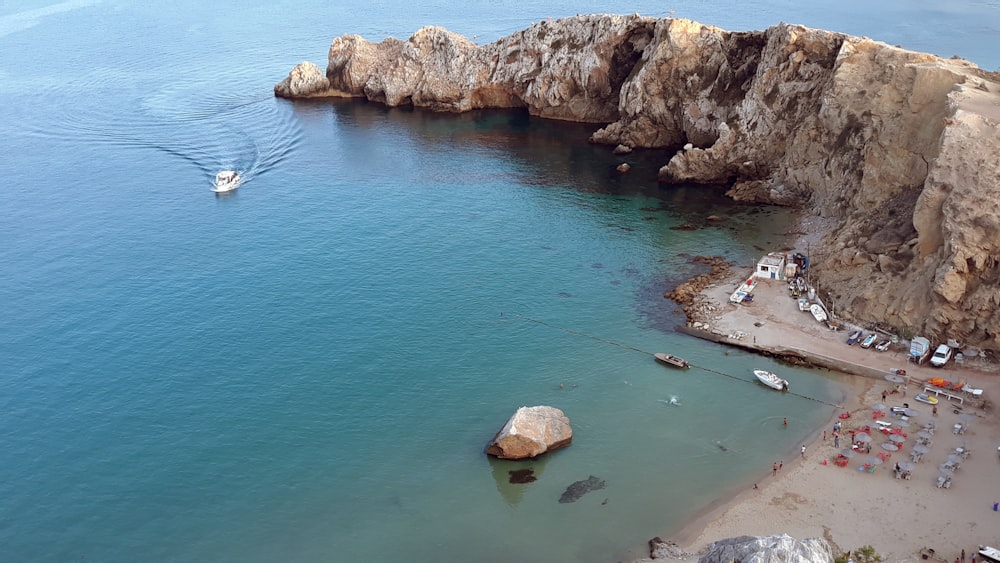 white boat on sea near brown rock formation during daytime