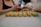 A person is preparing or arranging small cookie-like pastries on a baking tray lined with parchment paper. The pastries are neatly aligned in rows, showing a textured surface and a light golden color. The focus is on the pastries, with the person's blurred figure in the background.