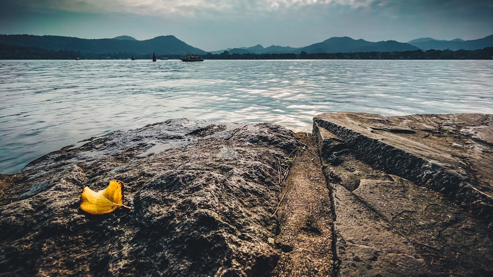 person in yellow hat sitting on rock near body of water during daytime