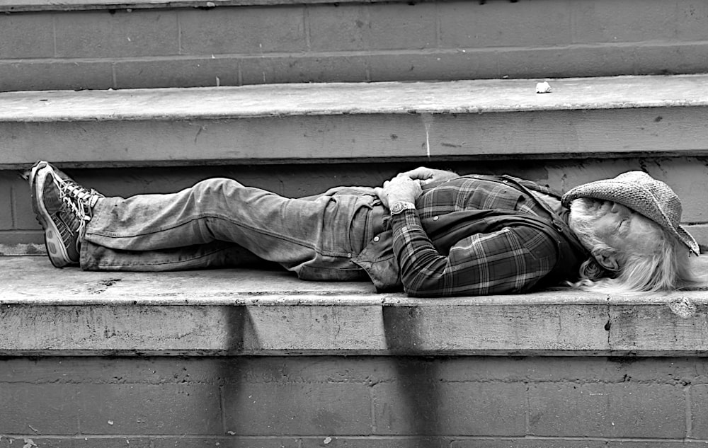grayscale photo of man in pants and jacket sitting on concrete stairs