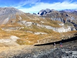 Majestic mountain landscape with rugged cliffs and expansive, rocky terrain. Two hikers are ascending a steep path under a clear blue sky, suggesting a sense of adventure and exploration.