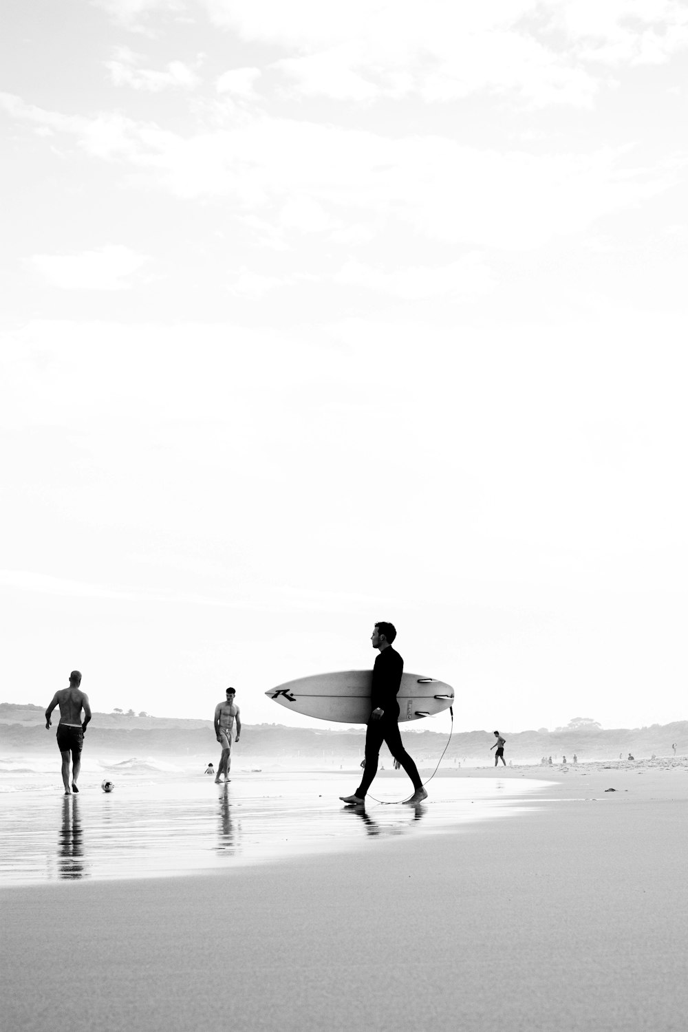 grayscale photo of man and woman holding surfboard walking on beach