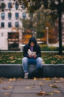 woman in blue denim jeans reading book sitting on blue concrete bench during daytime