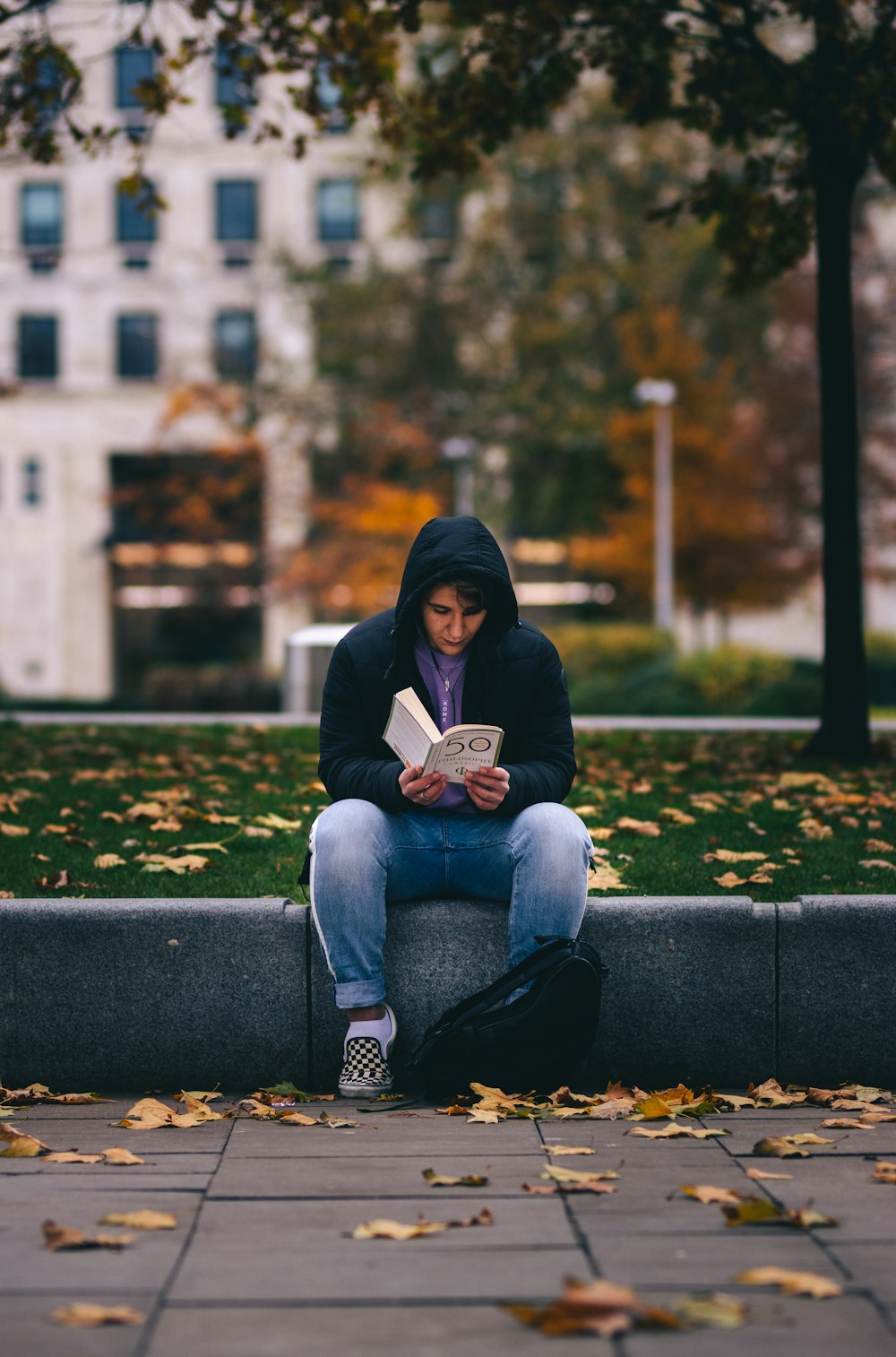 woman in blue denim jeans reading book sitting on blue concrete bench during daytime