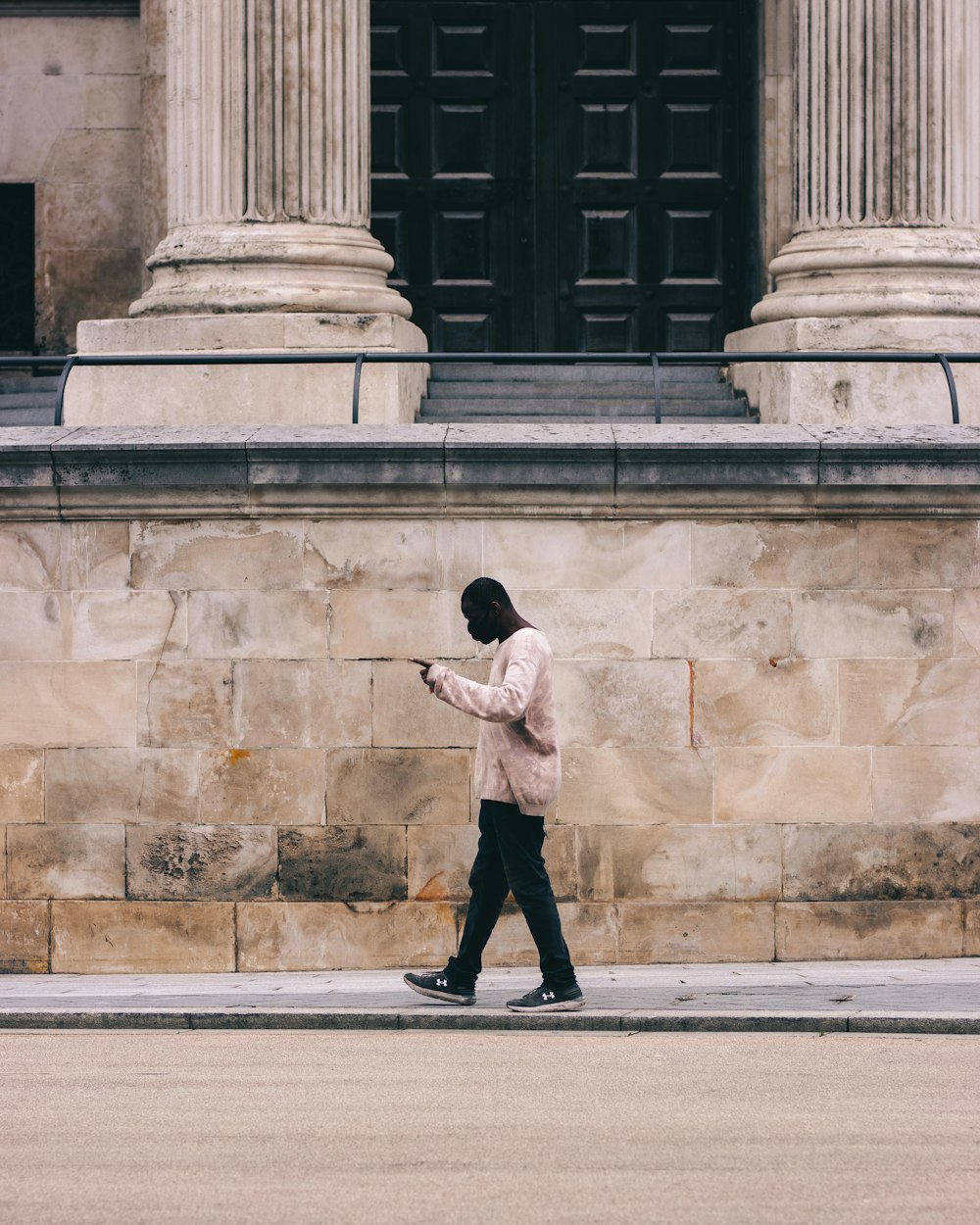 uomo in camicia bianca e pantaloni neri che cammina sul marciapiede durante il giorno