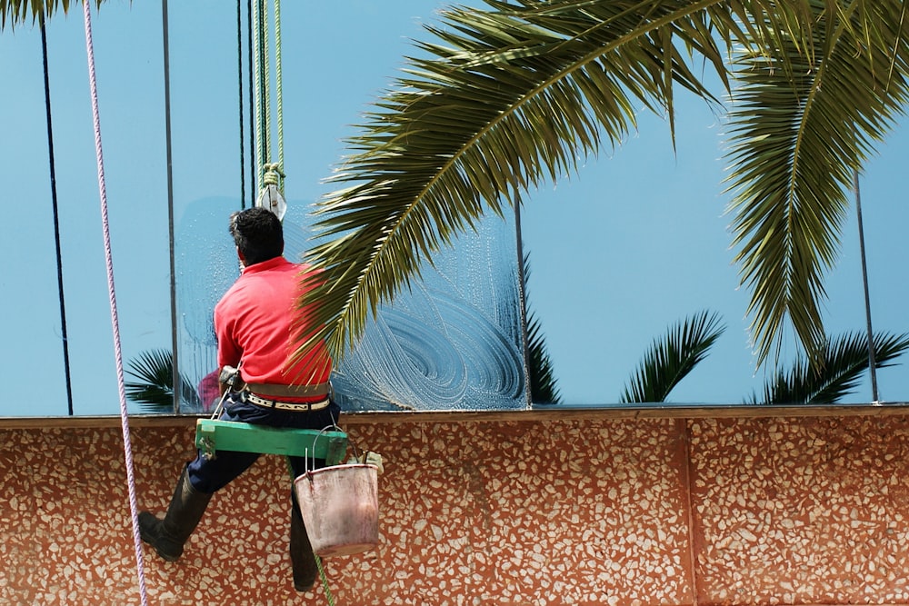 man in red t-shirt and green pants sitting on brown concrete bench during daytime