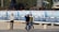 Several people are in an outdoor area near a construction site. One person in a striped sweater poses for a photograph while another holds a camera. Behind them are banners displaying images and text related to 'Estacionamiento Plaza de la República Siglo XXI'. Construction materials and equipment are visible in the background.