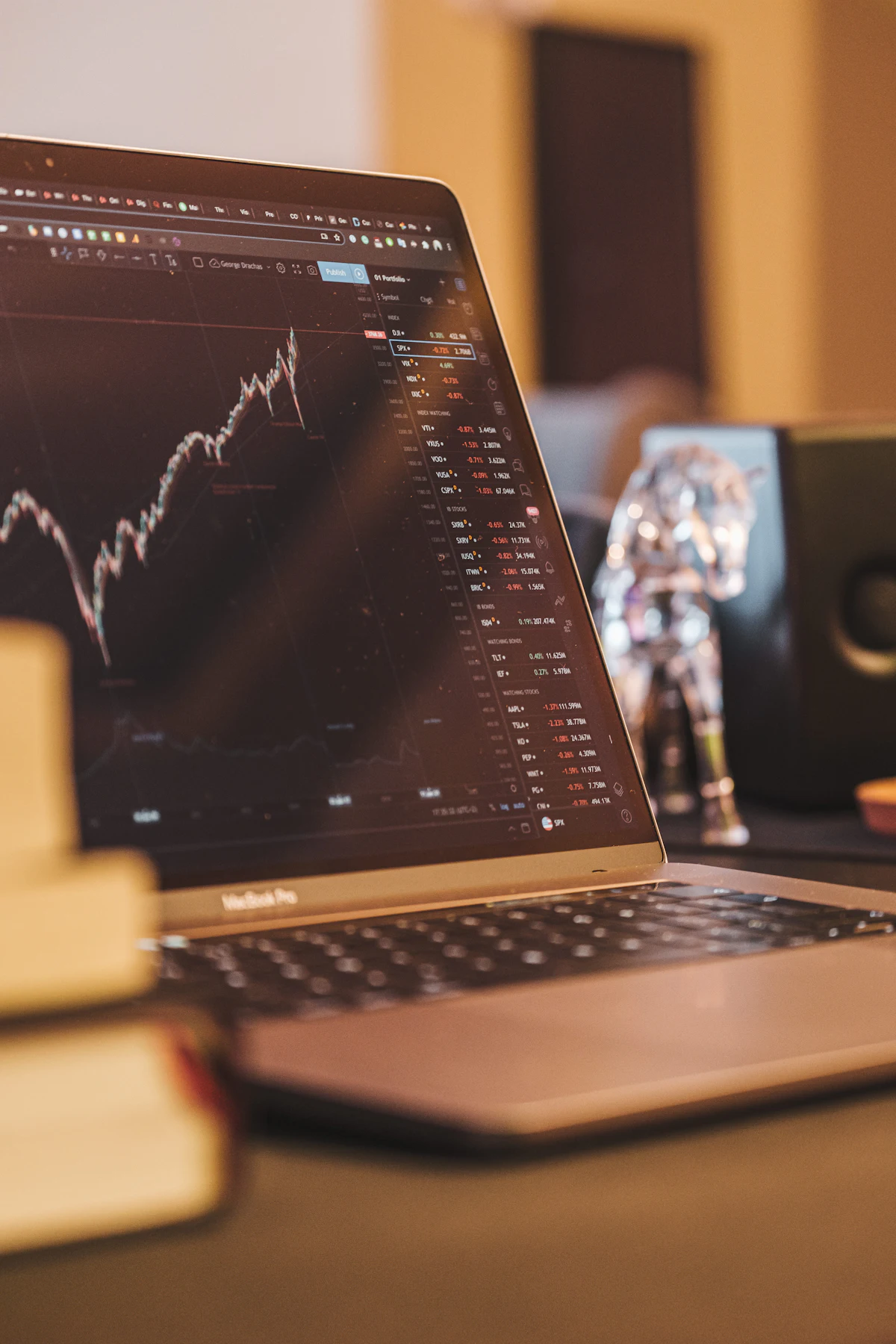Laptop menampilkan grafik analisis fundamental saham di meja kerja investor dengan dokumen laporan keuangan emiten dan kalkulator
