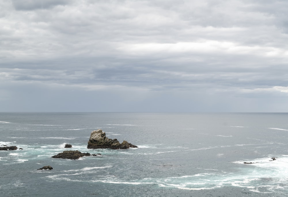 brown rock formation on sea under white clouds during daytime