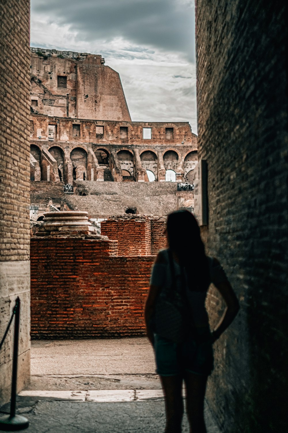 woman in black coat standing near brown brick wall during daytime