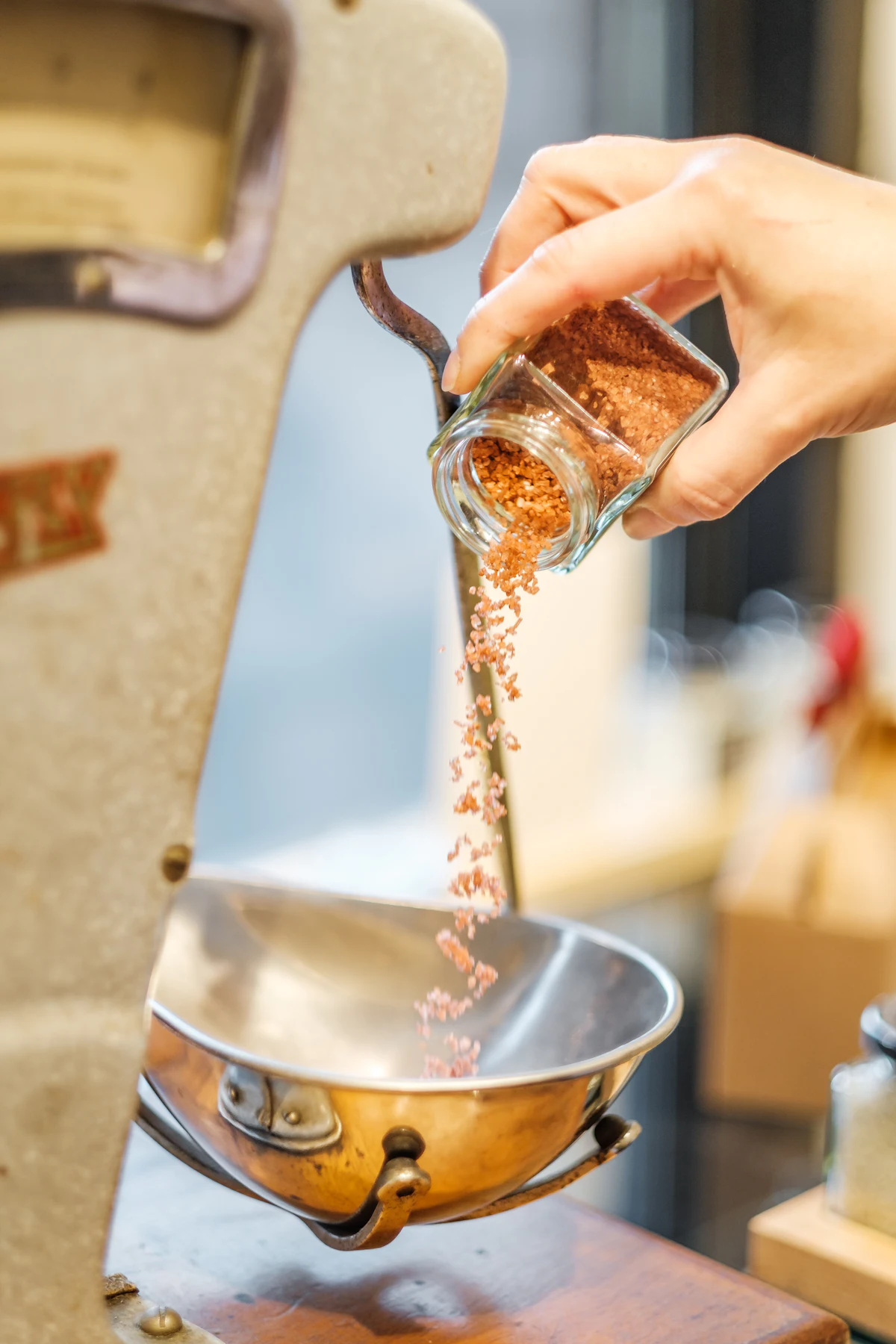 A person pouring water into a stainless steel mixing bowl, adjusting a dough's hydration