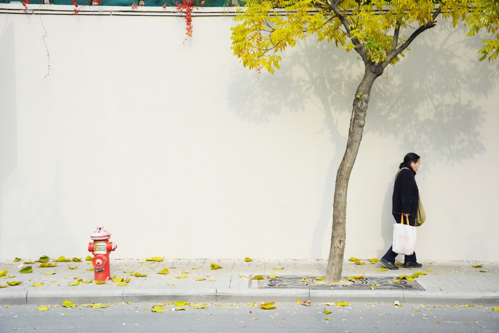 person in black jacket and white pants standing beside green tree during daytime