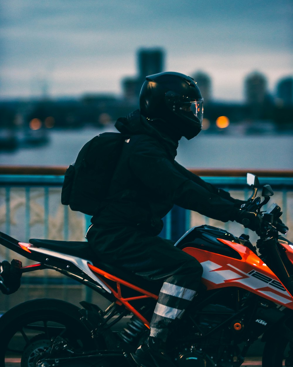 Hombre en chaqueta negra montando motocicleta naranja y negra