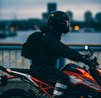 man in black jacket riding orange and black motorcycle